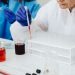 Female scientist in lab coat using pipette on test tubes, focusing on colorful chemical analysis.