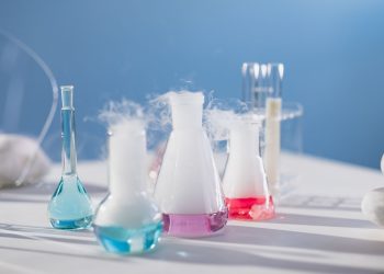 Brightly colored laboratory flasks emitting steam on a table, showcasing scientific exploration.