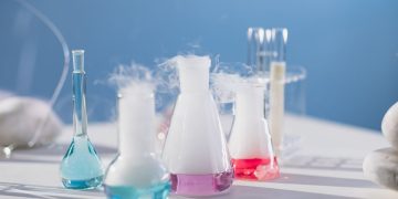 Brightly colored laboratory flasks emitting steam on a table, showcasing scientific exploration.