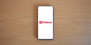Smartphone with Pinterest logo on screen placed on a wooden surface, minimalistic tech concept.