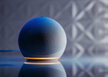 Close-up of a modern smart speaker in a stylish setting with illuminated base and reflection.