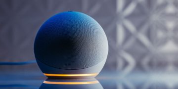 Close-up of a modern smart speaker in a stylish setting with illuminated base and reflection.