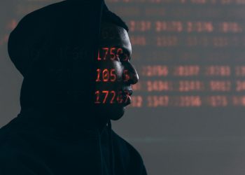 어두운 배경에서 붉은 데이터 코드가 얼굴에 투영된 후드를 쓴 인물, 데이터 프라이버시 위협을 상징