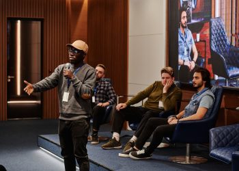 A group of diverse men engaging in a business conference with a speaker holding a microphone.