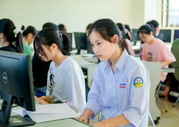 A group of students focused on computer screens in a modern classroom setting.