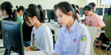 A group of students focused on computer screens in a modern classroom setting.