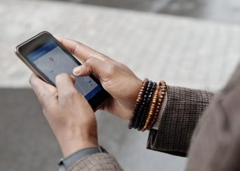 Close-up of hands with bracelets navigating on smartphone using GPS app outdoors.