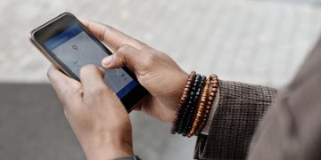 Close-up of hands with bracelets navigating on smartphone using GPS app outdoors.