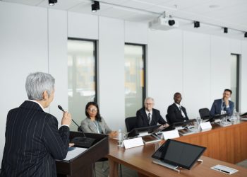 A diverse group of professionals engaging in a business meeting in a conference room with a speaker at the podium.
