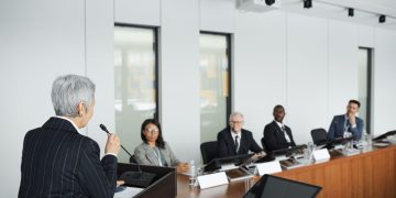 A diverse group of professionals engaging in a business meeting in a conference room with a speaker at the podium.