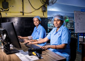 Two female workers at a textile factory operating computers in an industrial setting.