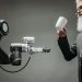 A bearded engineer holds a ceramic cup while a robotic arm assists, showcasing modern technology.