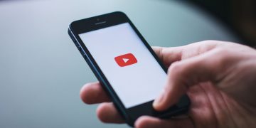 Close-up of a hand holding a smartphone displaying the YouTube app on the screen.