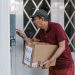 Man delivering a package at a front door, wearing a red shirt and cap.
