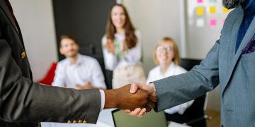 Close-up of a handshake between colleagues in a professional office setting, emphasizing teamwork and agreement.