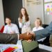 Close-up of a handshake between colleagues in a professional office setting, emphasizing teamwork and agreement.