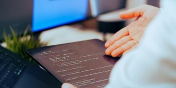 Software developer analyzing code on a tablet in a modern office workspace.