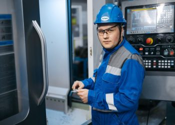 Industrial engineer in safety gear working on a CNC machine in a modern factory setting.