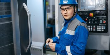 Industrial engineer in safety gear working on a CNC machine in a modern factory setting.