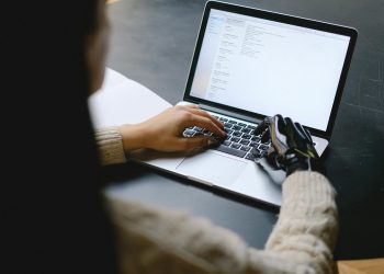 A person with a prosthetic hand using a laptop, showcasing technology and inclusivity.