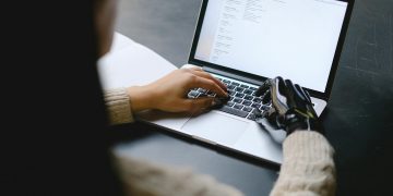 A person with a prosthetic hand using a laptop, showcasing technology and inclusivity.