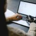 A person with a prosthetic hand using a laptop, showcasing technology and inclusivity.