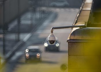 CCTV camera overlooking a busy street with cars in motion, capturing urban surveillance.