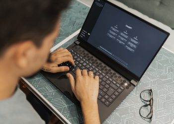 A man working on a laptop with AI software open on the screen, wearing eyeglasses.