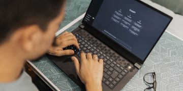 A man working on a laptop with AI software open on the screen, wearing eyeglasses.