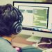 A programmer with headphones focuses on coding at a computer setup with dual monitors.