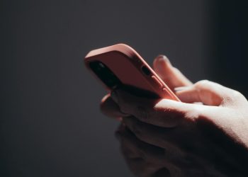 Close-up of hands holding a smartphone in dim lighting, showcasing texting or browsing activity.