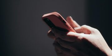 Close-up of hands holding a smartphone in dim lighting, showcasing texting or browsing activity.