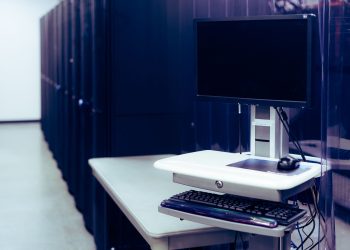 Contemporary computer with black screen placed on stand near row of server steel racks in data center