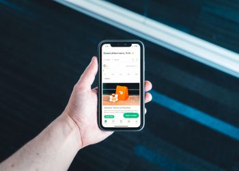 Hand holding smartphone with food delivery app on screen in bright setting.