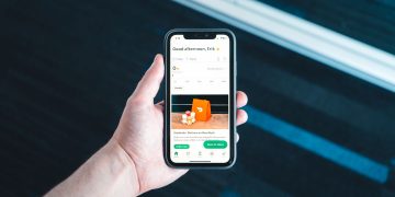 Hand holding smartphone with food delivery app on screen in bright setting.