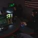 Cybersecurity professionals working on computer systems, focusing on data protection in a dimly lit room.