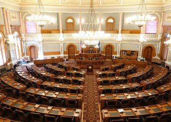Wide view of an ornate legislative chamber with empty seats and chandeliers.