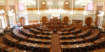 Wide view of an ornate legislative chamber with empty seats and chandeliers.