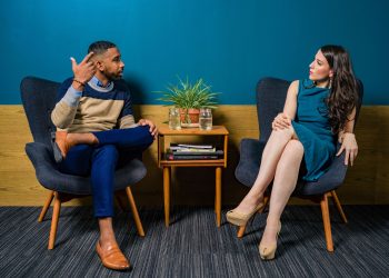 Two professionals in business attire engage in a thoughtful discussion sitting in a stylish, modern room.