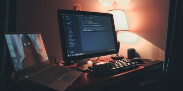 Warmly lit home office with dual screens for coding and programming. Perfect modern workspace for tech enthusiasts.