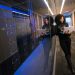 A woman using a laptop navigating a contemporary data center with mirrored servers.