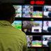 Man in a control room overseeing multiple monitors displaying various scenes.
