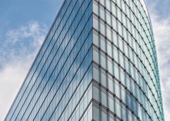 A sleek glass skyscraper reflecting the blue sky and clouds, showcasing modern architectural design.
