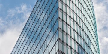 A sleek glass skyscraper reflecting the blue sky and clouds, showcasing modern architectural design.