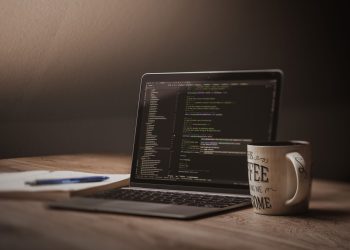 A comfortable workspace showcasing a laptop with code, a coffee mug, and a notepad.