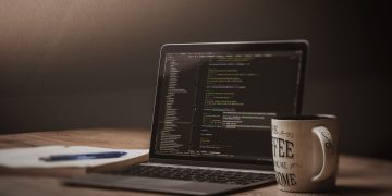 A comfortable workspace showcasing a laptop with code, a coffee mug, and a notepad.