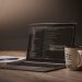 A comfortable workspace showcasing a laptop with code, a coffee mug, and a notepad.