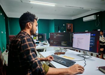 Software developer coding on dual monitors in a well-lit modern office, focused and engaged.