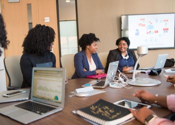 Four diverse women engaged in a business meeting with laptops and presentations in an office.