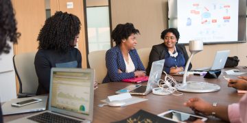Four diverse women engaged in a business meeting with laptops and presentations in an office.